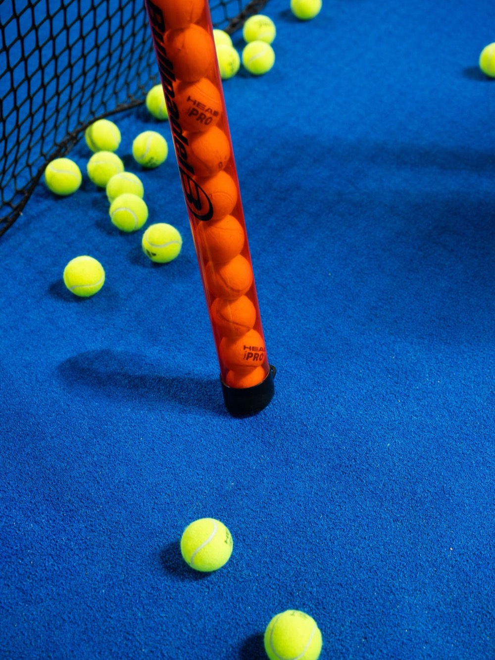 Padel balls and a ball tube on a blue court – Padel