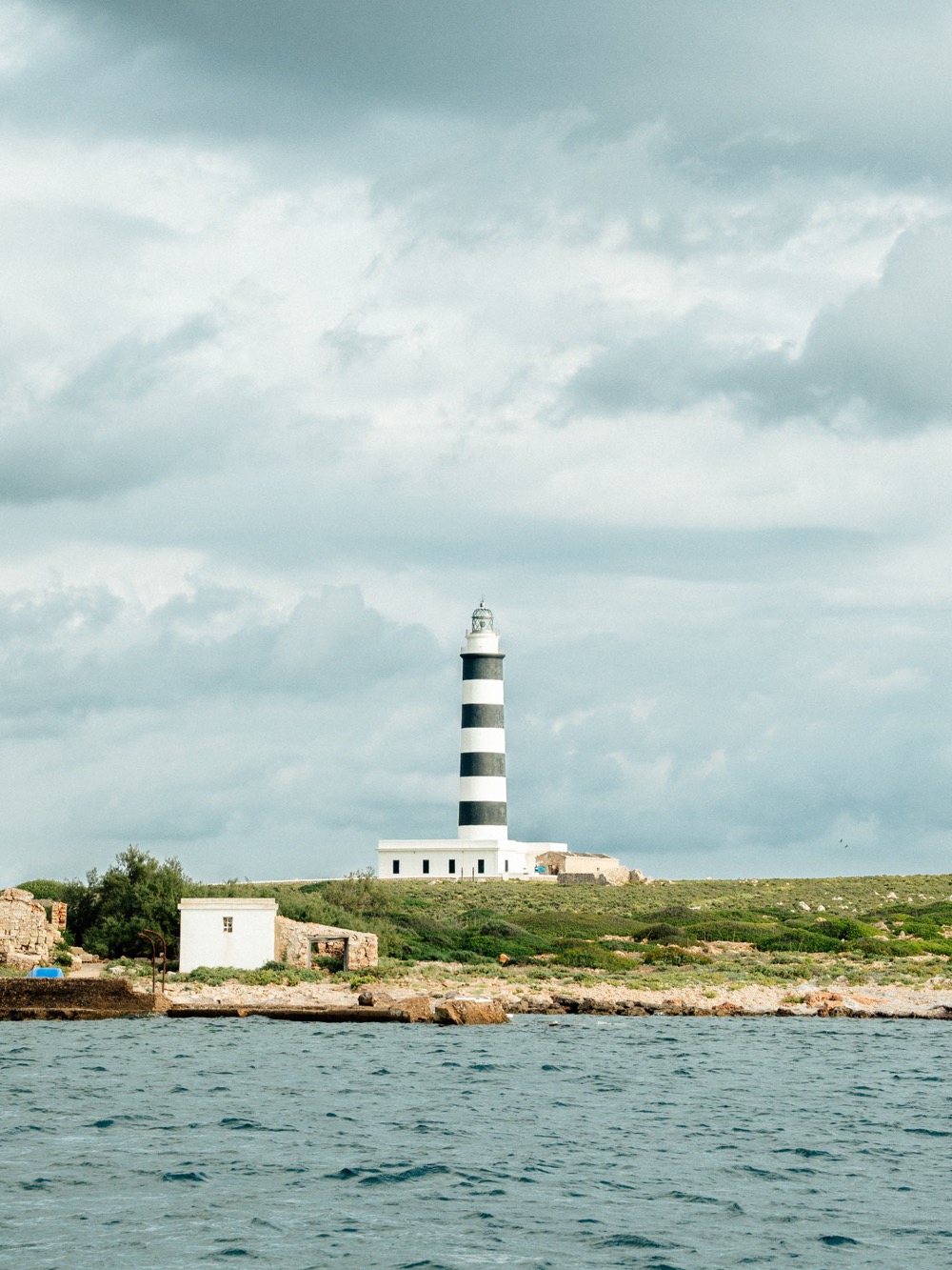 A black-and-white striped lighthouse on the shore – Menorca coast